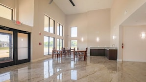 Un'ampia hall con pavimento in marmo, ampie finestre, un'area ristorazione con tavoli e sedie, e un segnale di uscita.