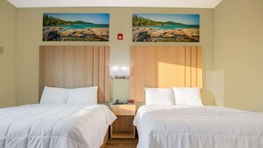 A hotel room with two beds, wooden headboards, a nightstand with a lamp, and a painting of a beach scene on the wall. - 2 Queen Beds Non-Smoking (Adairsville GA)