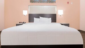 A hotel room with a large bed, two bedside tables, a headboard, and a painting on the wall. - King Bed Non-Smoking (Adairsville GA)