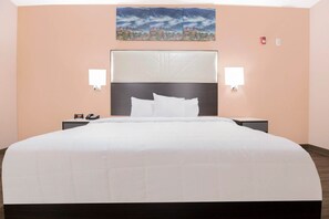 A hotel room with a large bed, two bedside tables, a headboard, and a painting on the wall. - King Bed Non-Smoking (Adairsville GA)