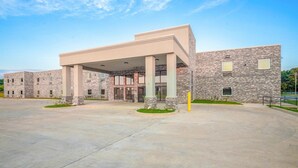 A modern building with a covered entrance, stone facade, and a spacious parking area. - King Bed Non-Smoking (Adairsville GA)