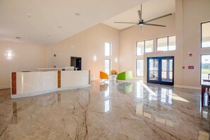 A spacious lobby with a reception desk, a ceiling fan, and large windows allowing natural light. - King Bed Non-Smoking (Adairsville GA)