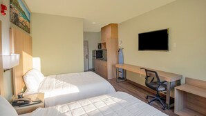 Een hotelkamer met twee bedden, een bureau, een stoel, een televisie en een kitchenette.