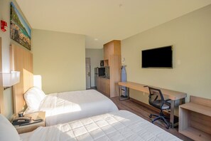 Ein Hotelzimmer mit zwei Betten, einem Schreibtisch, einem Sessel, einem Fernseher und einer Küchenzeile.