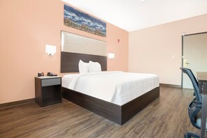 A hotel room with a bed, nightstand, wall-mounted lamp, and a mirror.
