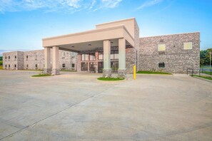 A modern building with a covered entrance, stone facade, and a large parking area.