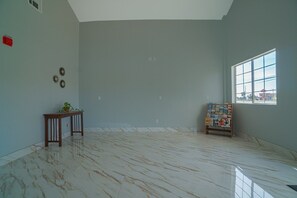 Una habitación con suelo de mármol, una pequeña mesa de madera con una planta, un adorno en la pared y una ventana con vistas.