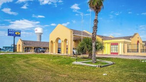 Ein Hotel mit gelber Fassade, einem Schild für Aransas Bay Inn & Suites und einem Wasserturm im Hintergrund.