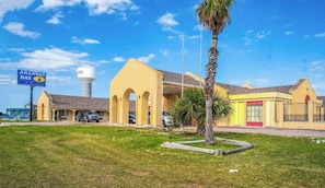 Un hotel con fachada amarilla, un letrero de Aransas Bay Inn & Suites, y una torre de agua al fondo.