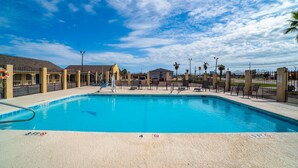 A swimming pool with lounge chairs and a fence. - 2 Bedroom Apartment without Kitchenette (Corpus Christi TX)