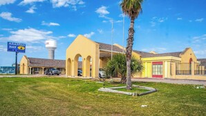 A hotel with a yellow facade, a signboard for Aransas Bay Inn & Suites, and a water tower in the background. - 2 Bedroom Apartment without Kitchenette (Corpus Christi TX)
