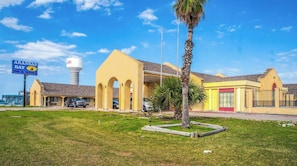 Un hotel con fachada amarilla, un letrero de Aransas Bay Inn & Suites, y una torre de agua al fondo.