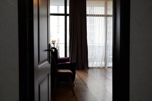 A room with a large window, a chair, and a table with a vase. - Hotel Lord (Batumi)