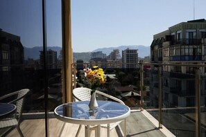 A balcony with a glass table and chairs, a vase with flowers, and a cityscape view. - Hotel Lord (Batumi)