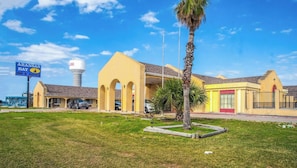 Un hôtel à la façade jaune, une enseigne indiquant « Aransas Bay Inn & Suites », et un château d’eau en arrière-plan.