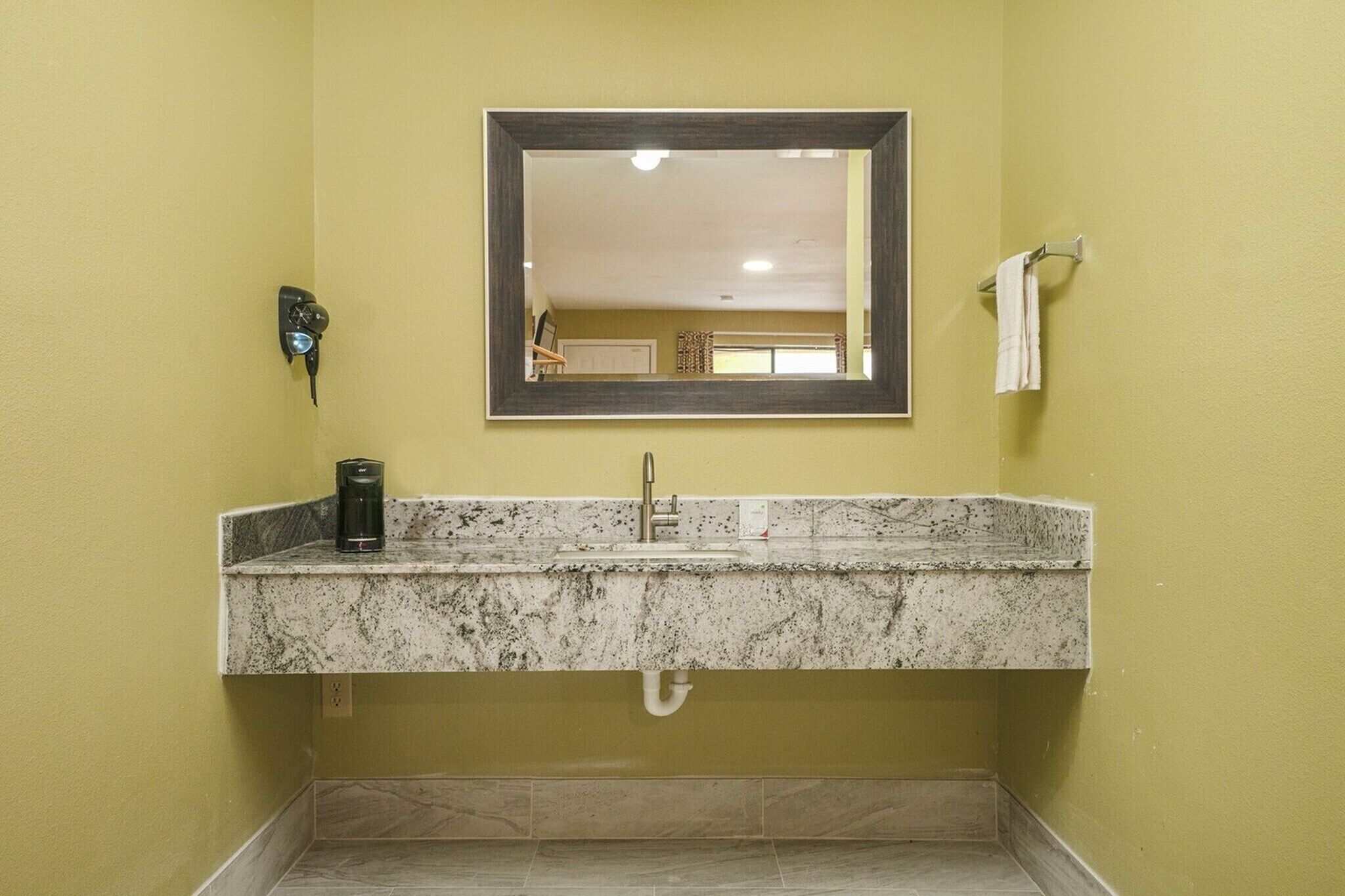 A bathroom with a granite countertop sink, a mirror, a towel rack, and a wall-mounted phone.