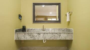A bathroom with a granite countertop sink, a mirror, a towel rack, and a wall-mounted phone.