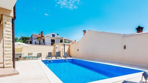 En swimmingpool med solstolar, en stenmur och en byggnad i bakgrunden.