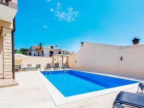 Ein Pool mit Liegestühlen, einer Steinmauer und einem Gebäude im Hintergrund.