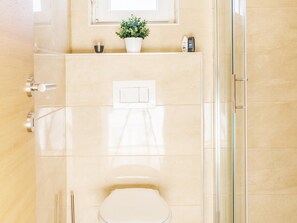 Ein Badezimmer mit Toilette, Dusche, Spiegel und einer Zimmerpflanze.