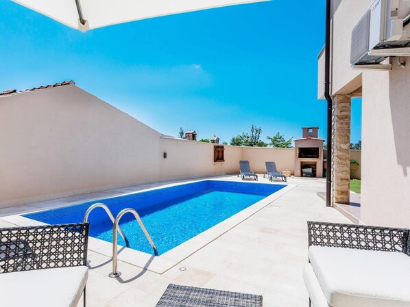 Ein Schwimmbecken mit Liegestühlen und einer überdachten Terrasse.