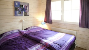 A bedroom with a bed, a window with curtains, a radiator, and a wall-mounted painting. - Fin Maison Sauna 4 (Belfeld)