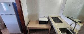 Une cuisine compacte équipée d’un réfrigérateur, d’un four à micro-ondes posé sur une petite table, d’une cuisinière à gaz et d’un évier.