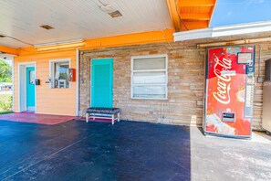 Un bâtiment avec un distributeur automatique de Coca-Cola, un banc et une porte dotée d’un volet bleu.