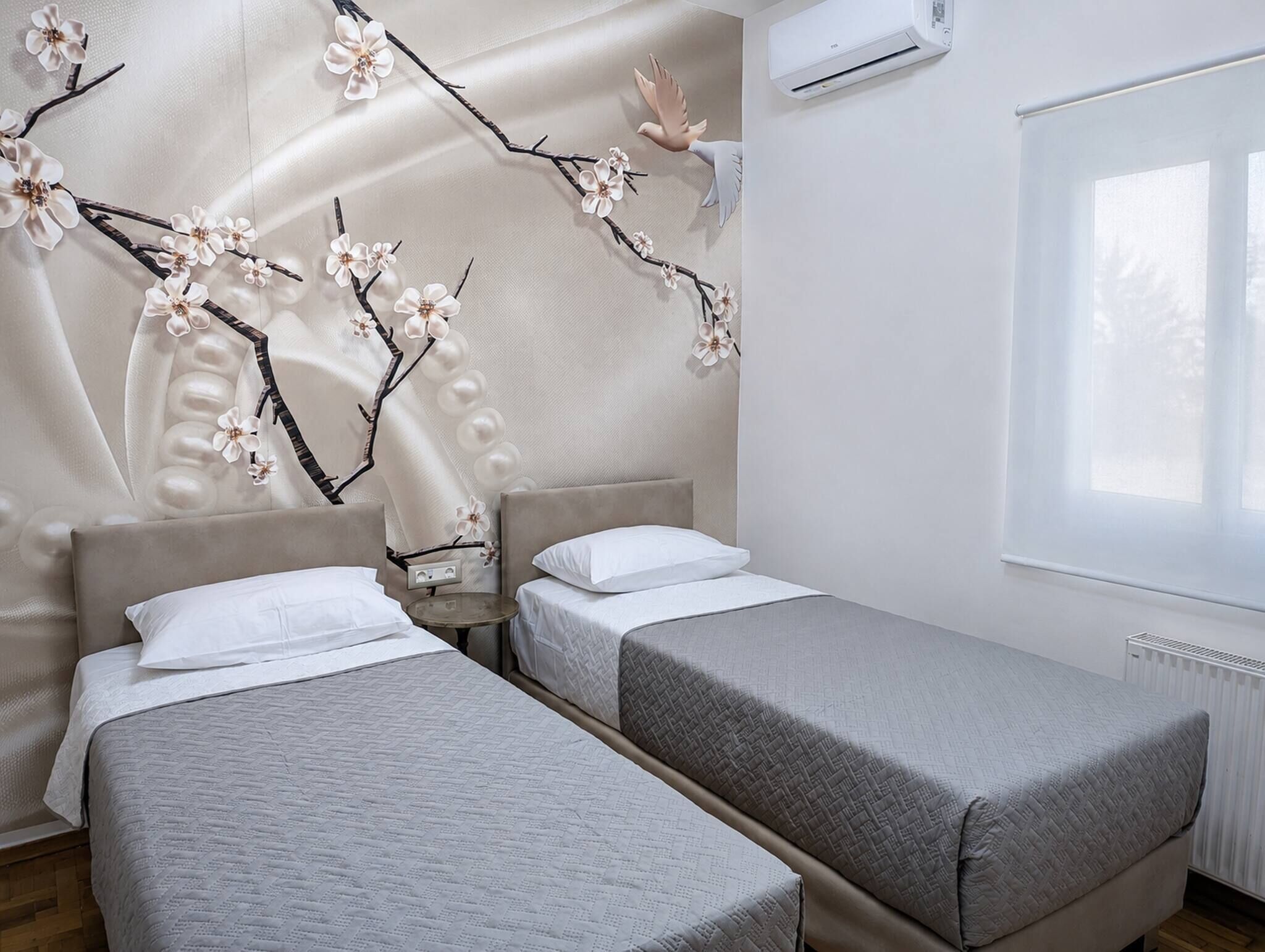 A hotel room with two beds, a wall-mounted air conditioner, and a window with a view.