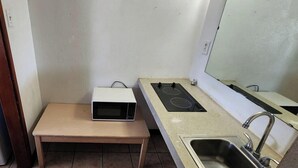 Uma cozinha compacta com geladeira, micro-ondas sobre uma mesinha, fogão a gás e pia.