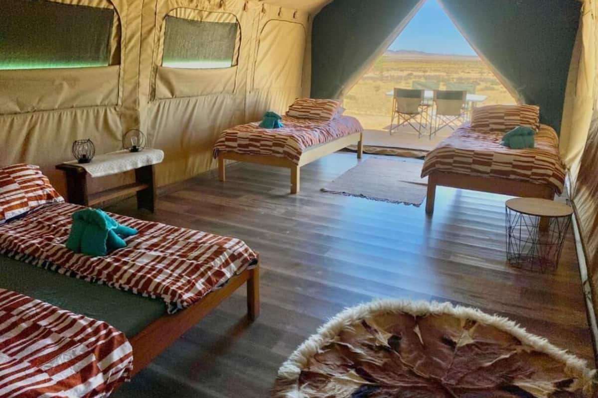 A tent with two beds, a small table, and a view of the desert.