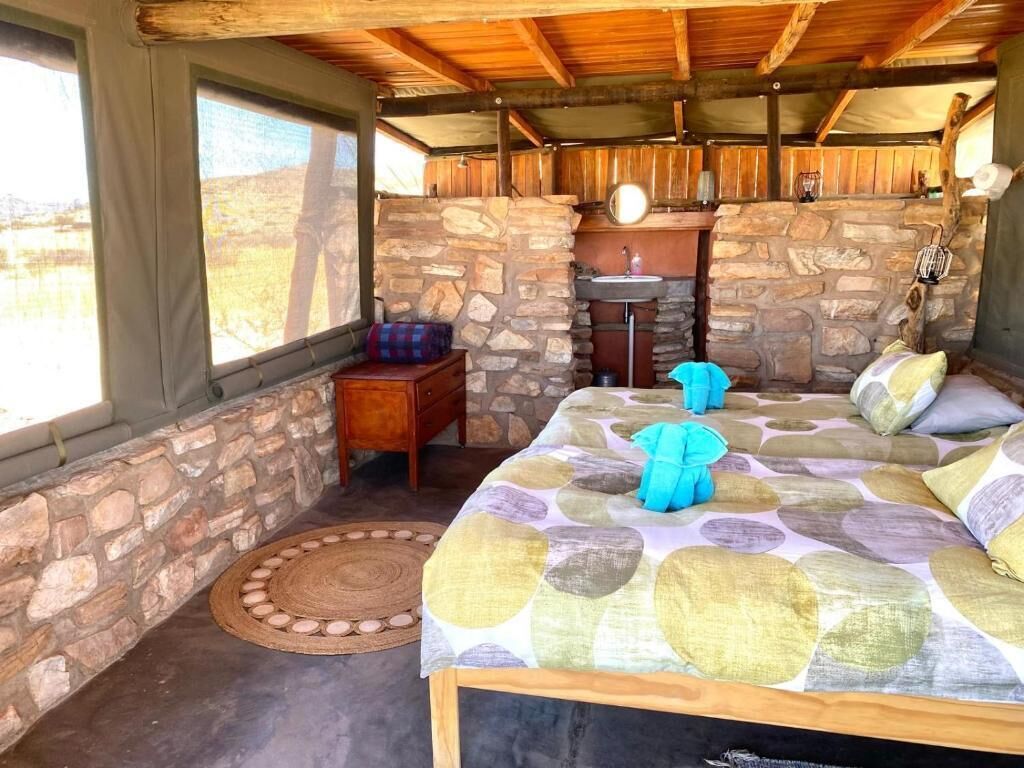 A rustic room with a stone wall, a bed with a patterned bedspread, a wooden ceiling, and a window overlooking a natural landscape.