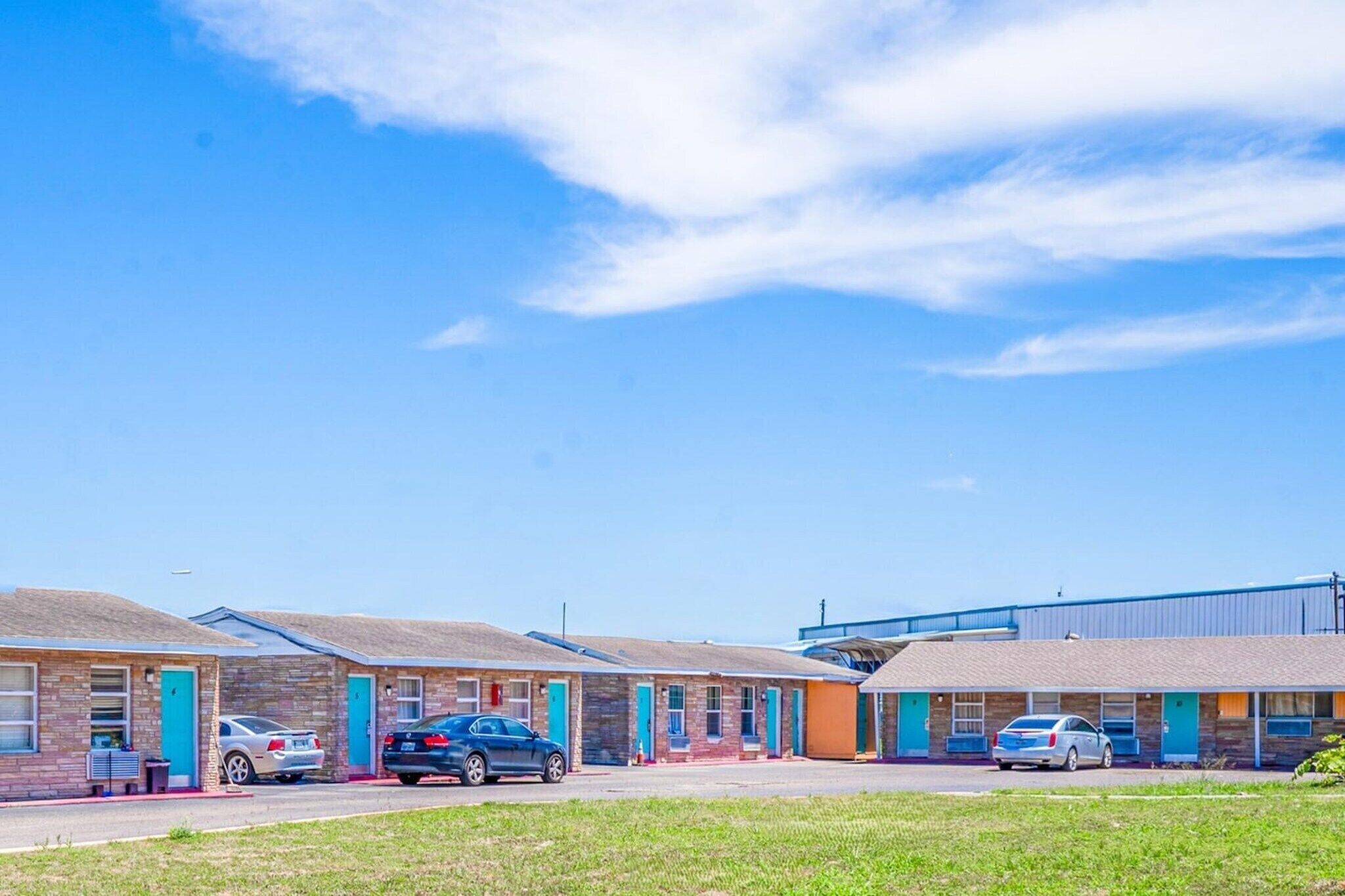 A motel with multiple rooms, each with a door and windows, and a parking area with cars.