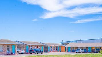 A motel with multiple rooms, each with a door and windows, and a parking area with cars.