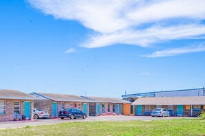 Ein Motel mit mehreren Zimmern, jedes mit Tür und Fenstern, sowie ein Parkplatz mit Autos.