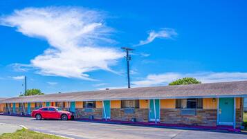 A motel with a row of rooms, a parking lot, and a red car parked in front.