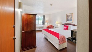 A hotel room with a bed, bedside lamps, a television, a wardrobe, and a window with curtains.