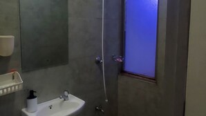 Un baño con un lavabo blanco, un cabezal de ducha de mano y una ventana con iluminación azul.
