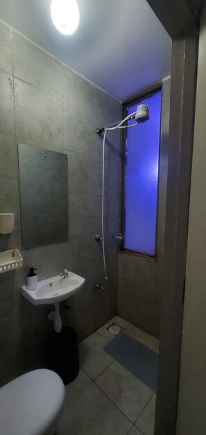 Casa de banho com uma pia branca, chuveiro manual e janela iluminada em azul.