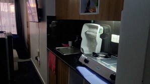 Una cocina compacta con armarios de madera, una estufa a gas, un lavamanos y un televisor montado en la pared.