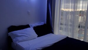 Una habitación de hotel con una cama, una luz nocturna, una ventana con cortinas y vistas a edificios.