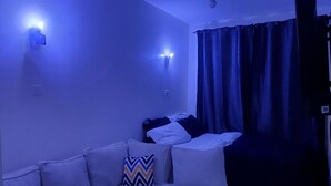 Una habitación con un sofá blanco modular, un control remoto en el reposabrazos y una cortina.
