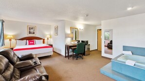 Habitación de hotel con cama, escritorio, silla, sillón de masaje, bañera y espejo.
