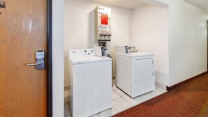 Un lavadero con lavadora y secadora Whirlpool, dispensador de jabón y un cartel que indica la disponibilidad de jabón, lejía y limpiador.