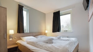 Une chambre d’hôtel avec un lit, des tables de chevet, des lampes, une fenêtre et un miroir.