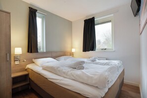 Ein Hotelzimmer mit einem Bett, Nachttischen, Lampen, einem Fenster und einem Spiegel.