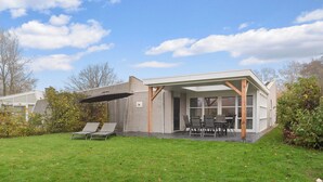 Une maison moderne dotée d’un patio couvert, d’une pelouse et d’un jardin.