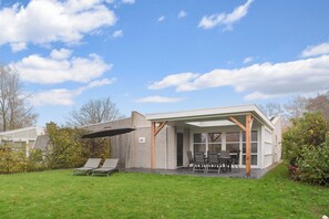 Ein modernes Haus mit überdachter Terrasse, Rasen und Garten.