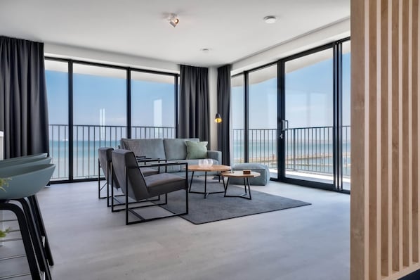 A modern living room with a sofa, chairs, a coffee table, and a view of the sea through large windows. - Waterfront Apartment Near Beach (Breskens)