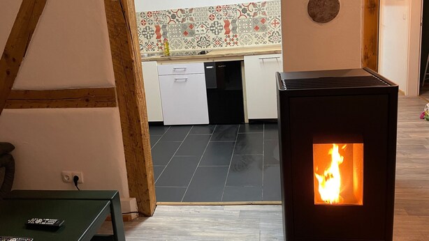 A modern kitchen with a tiled backsplash, a black stove with a visible flame, and a wooden ceiling.